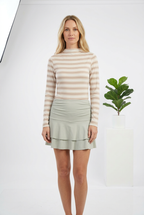 Donna con capelli lunghi biondi e il completo della foto, su sfondo bianco con una pianta verde di lato